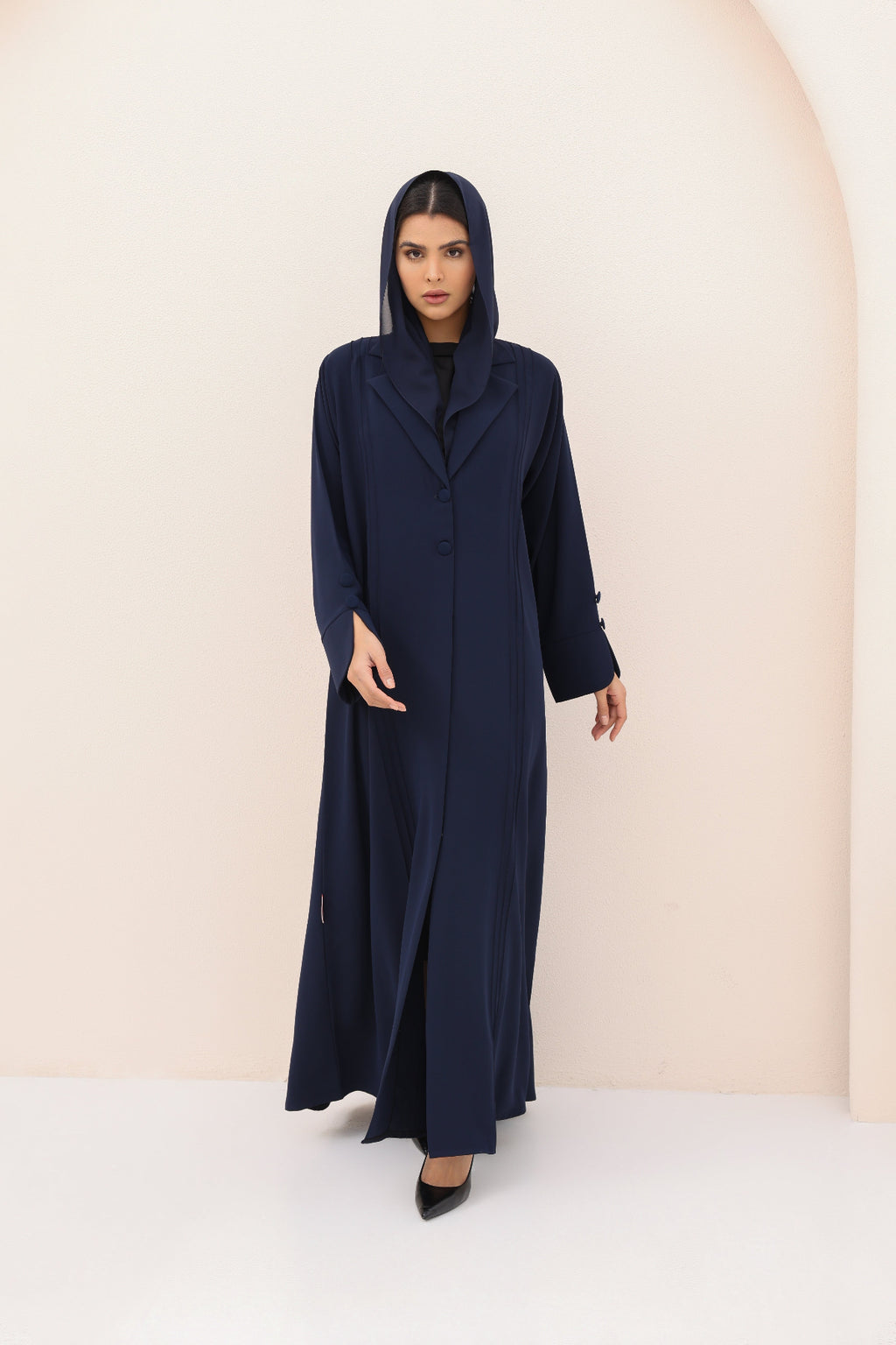 Woman wearing a long navy blue dress with a hood against a beige background