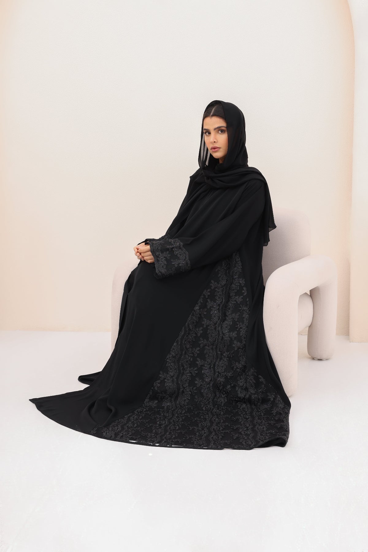 Woman wearing a black abaya with floral patterns on a white background