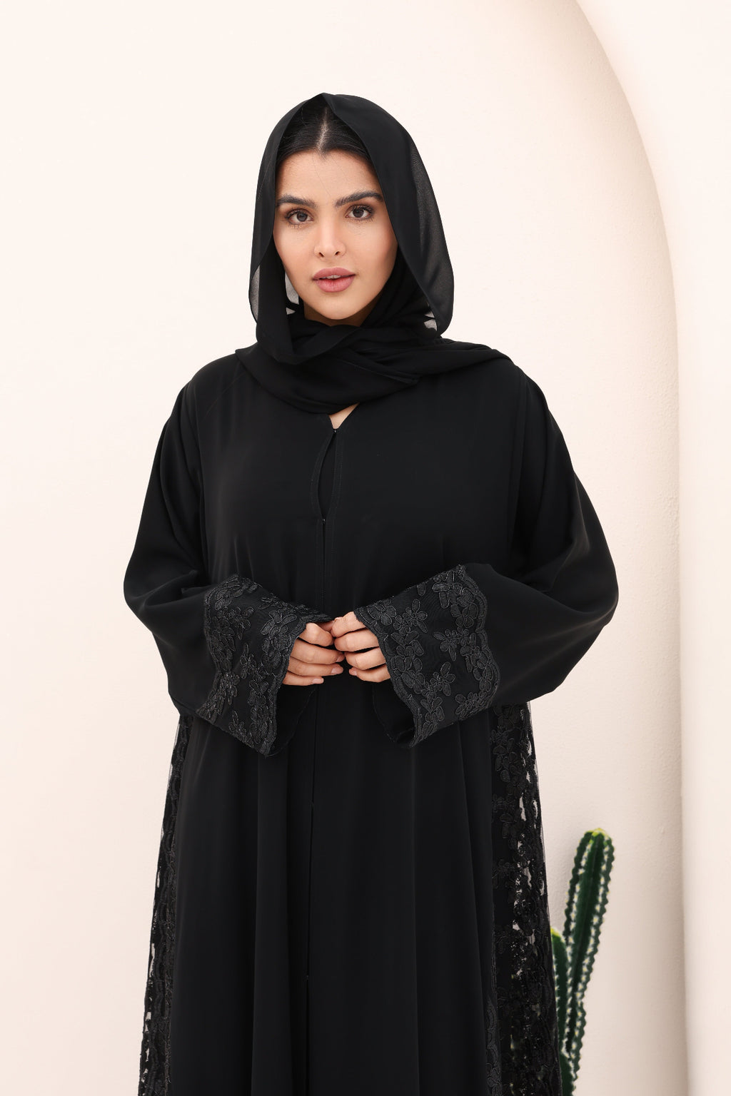 Woman wearing a black abaya with lace details on a beige background