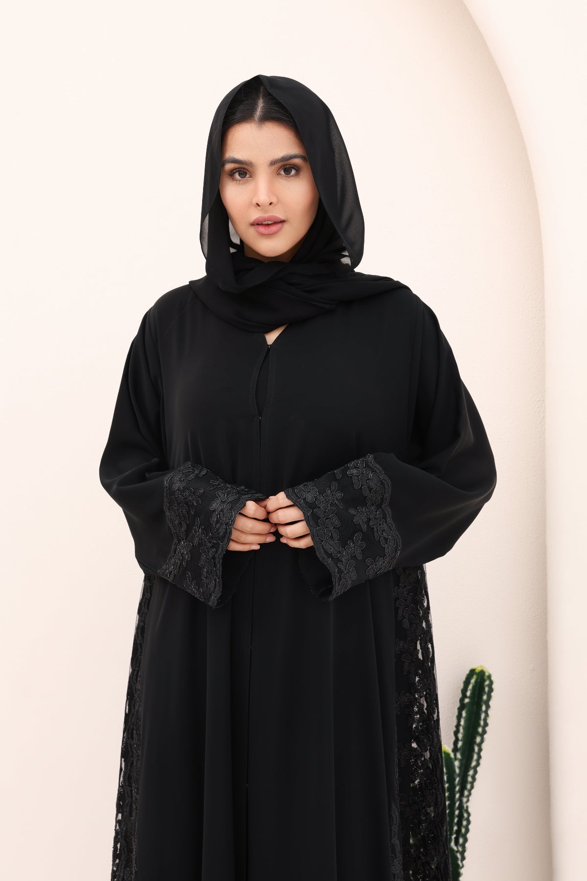 Woman wearing a black abaya with lace details on a beige background