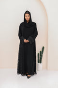 Woman wearing a black abaya with lace details against a white background