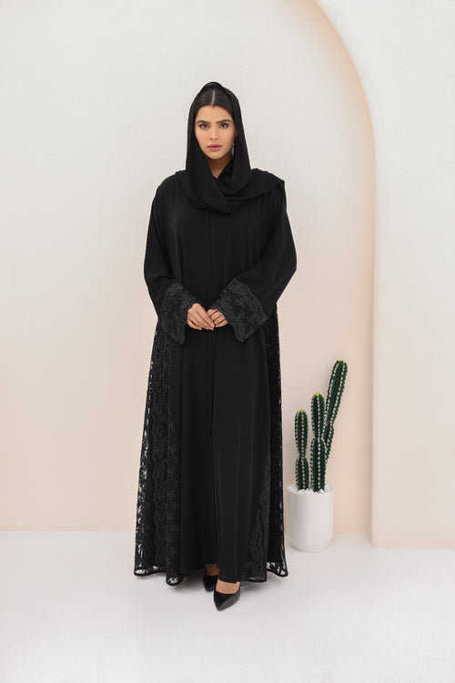 Woman wearing a black abaya with lace details against a white background