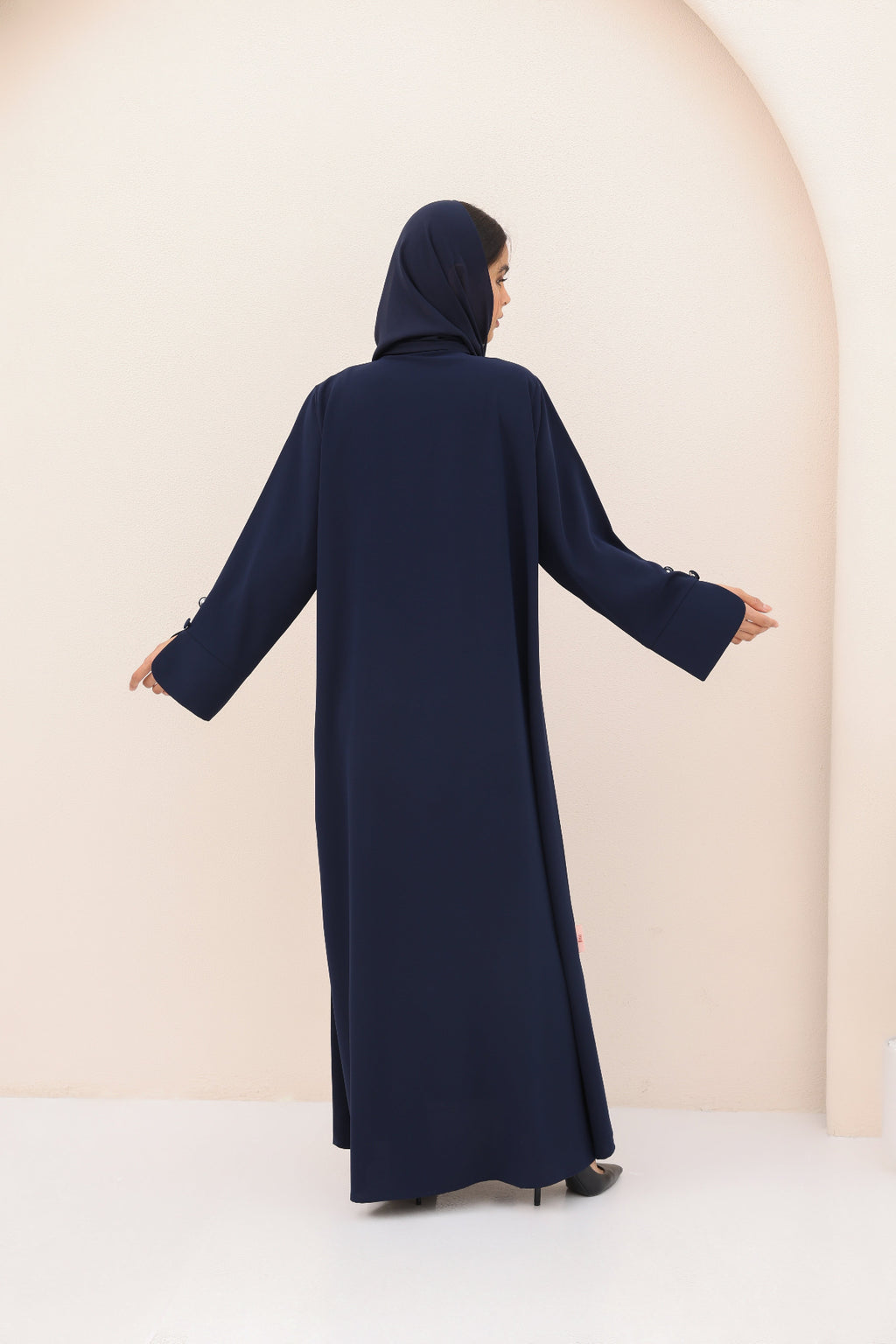 Person wearing a navy blue abaya against a beige background