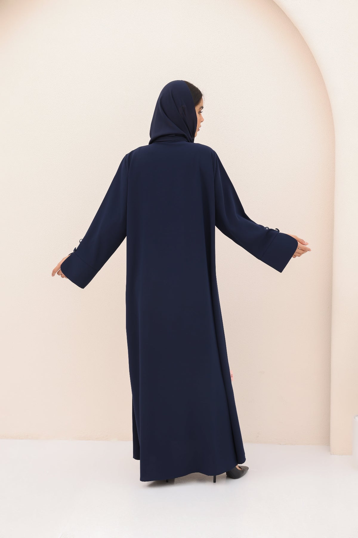 Person wearing a navy blue abaya against a beige background