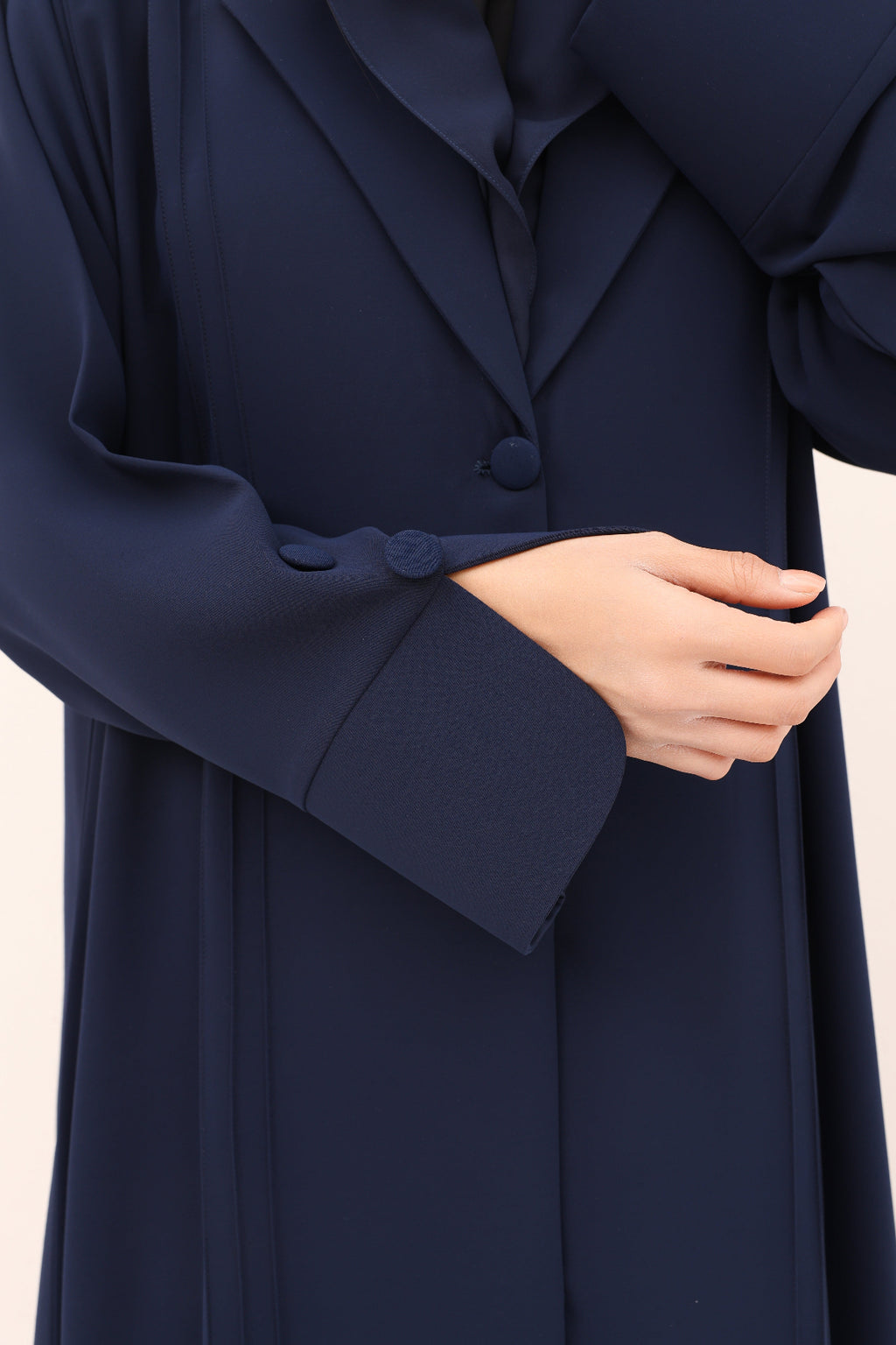 Navy blue coat with a hand adjusting the sleeve on a beige background