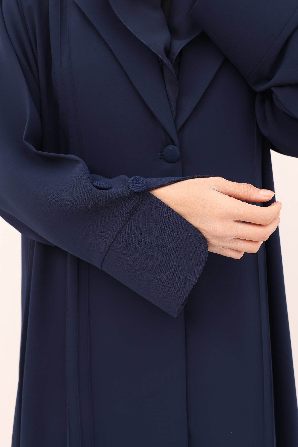 Navy blue coat with a hand adjusting the sleeve on a beige background