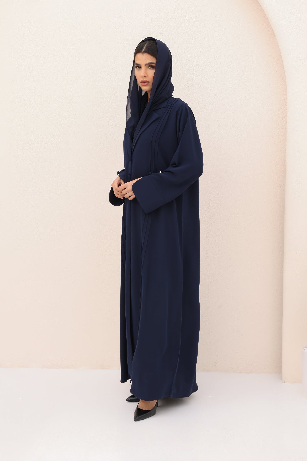 Woman wearing a navy blue abaya against a beige background