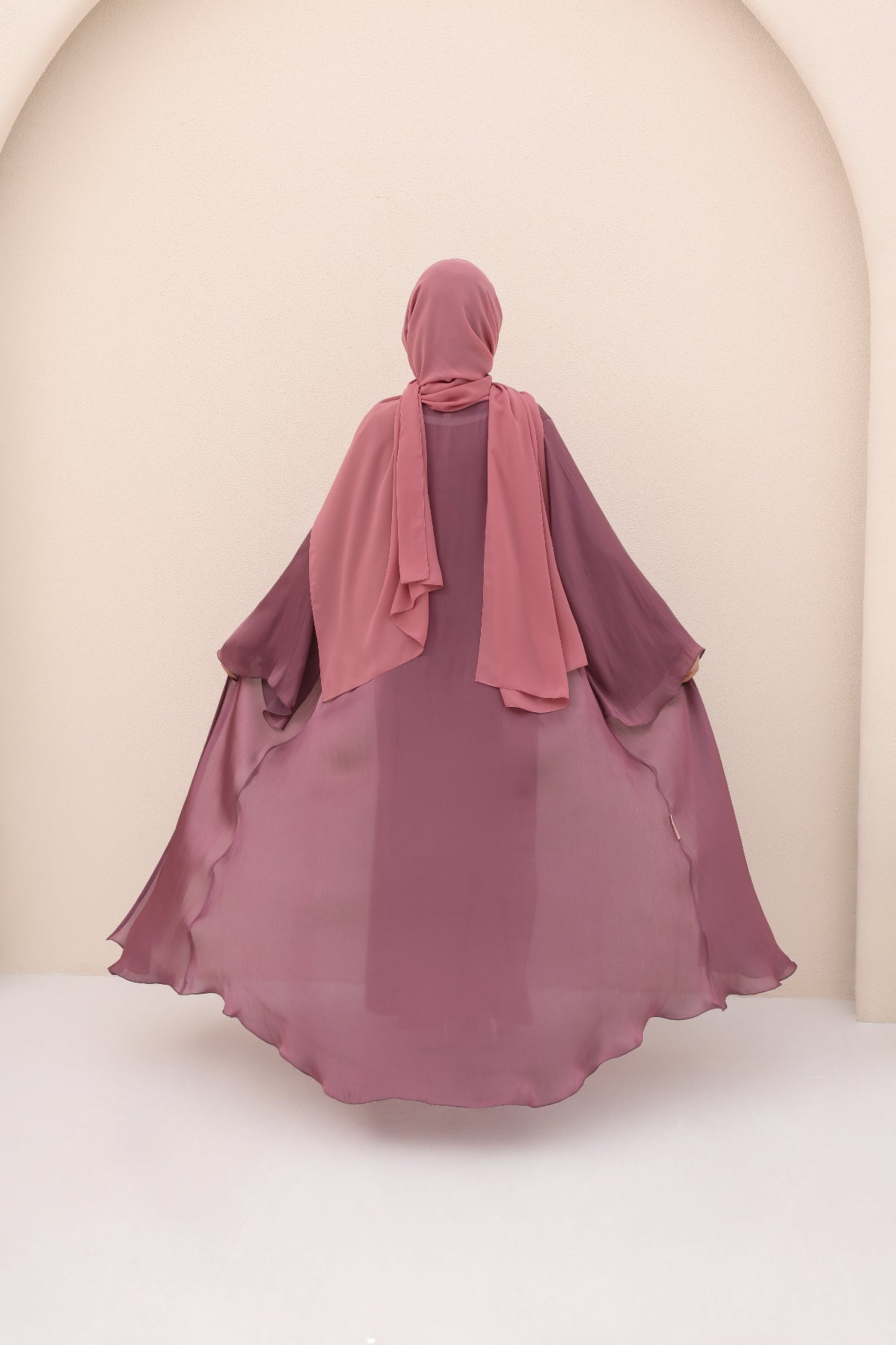 Person wearing a mauve dress with a matching hijab in a neutral setting