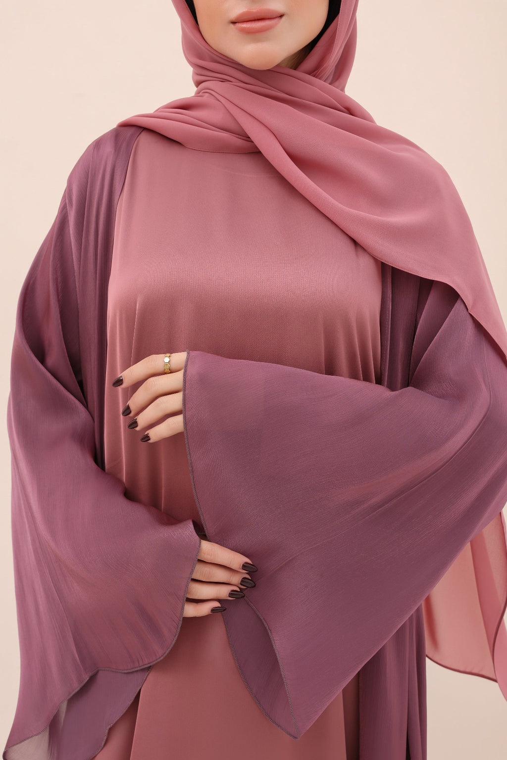 Person wearing a mauve abaya with a matching hijab on a beige background