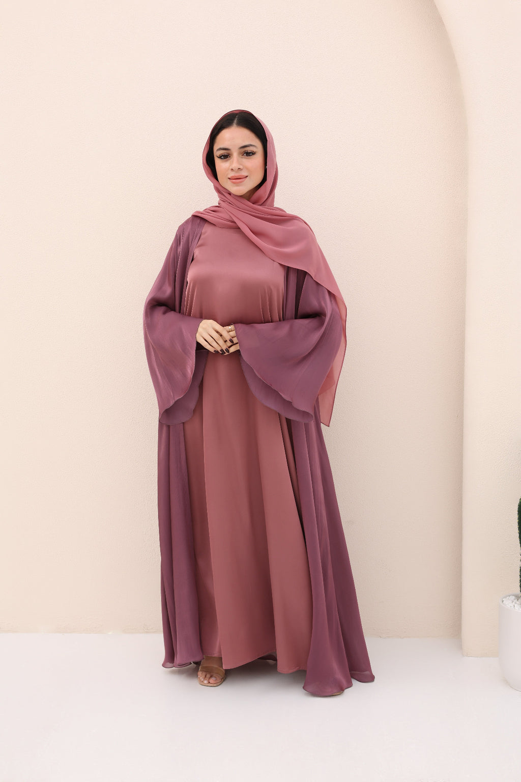Woman wearing a mauve abaya and hijab against a beige background