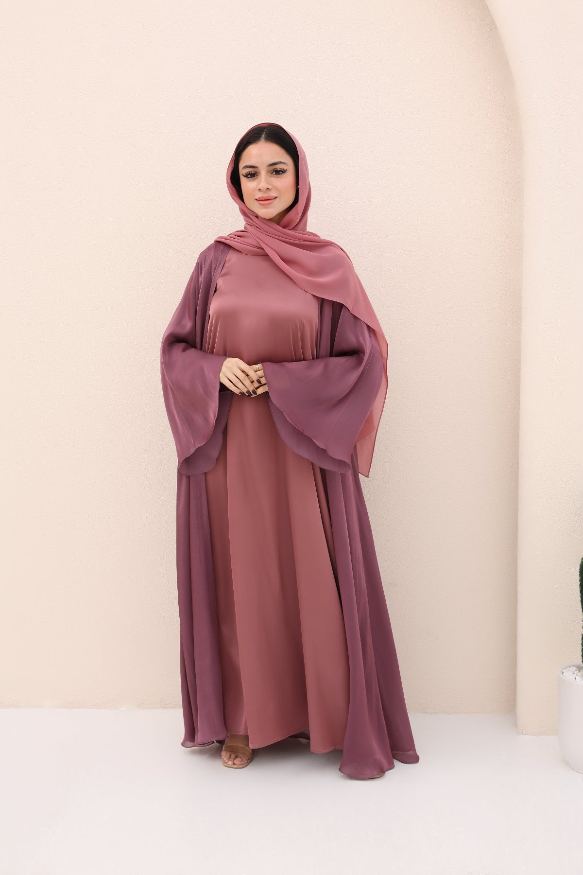 Woman wearing a mauve abaya and hijab against a beige background