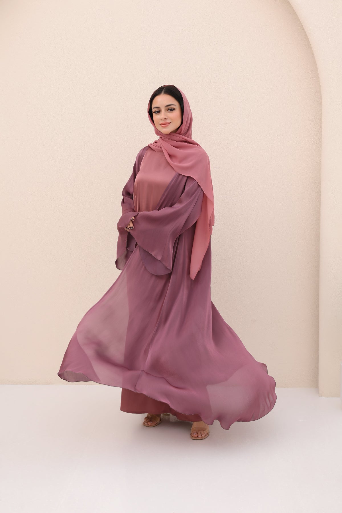 Woman wearing a long, flowing dress with a matching hijab against a neutral background
