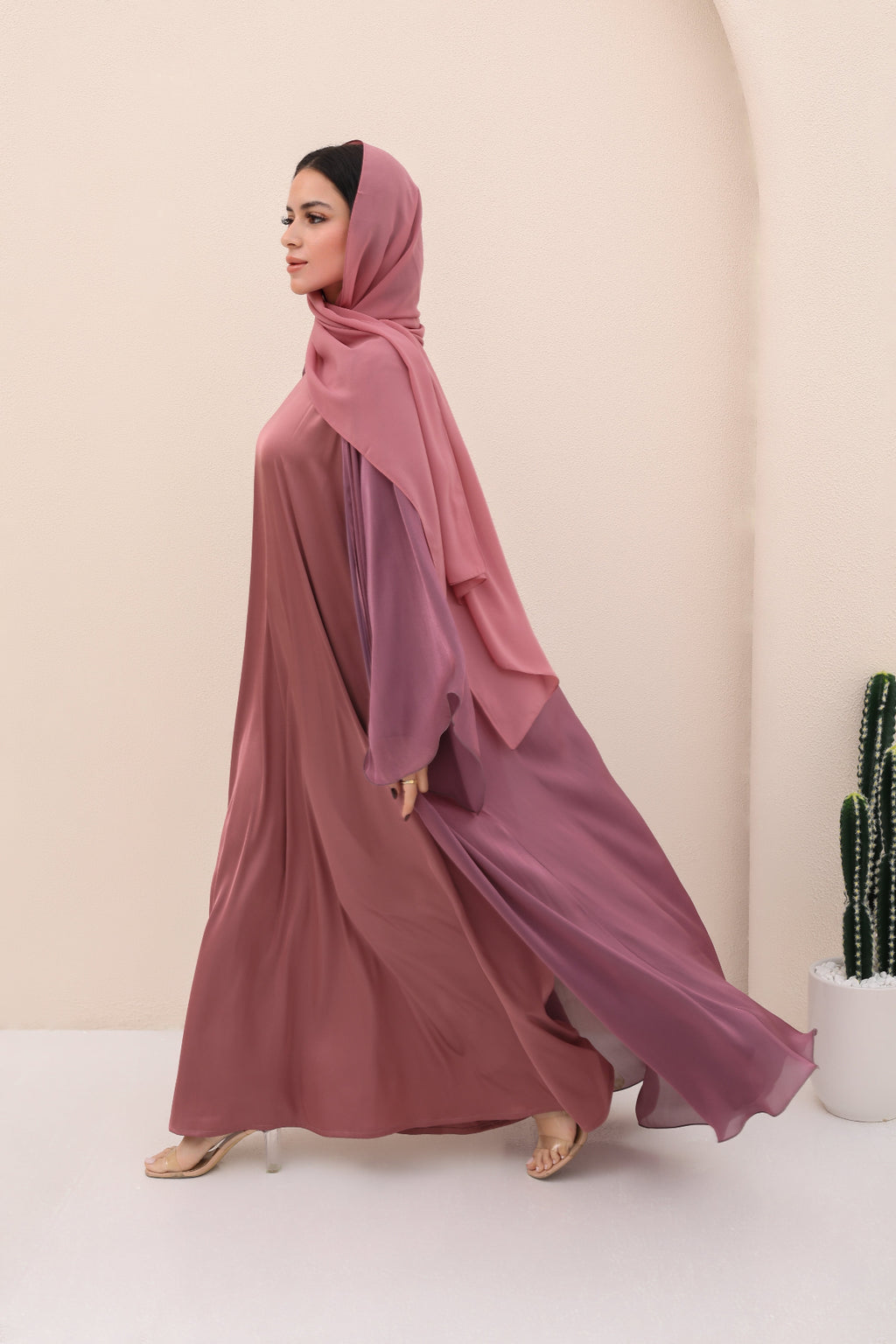 Woman wearing a long, flowing dress with a matching hijab against a plain background
