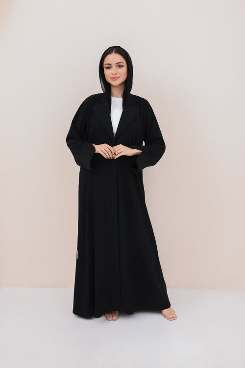 Woman wearing a black abaya with a white top on a beige background