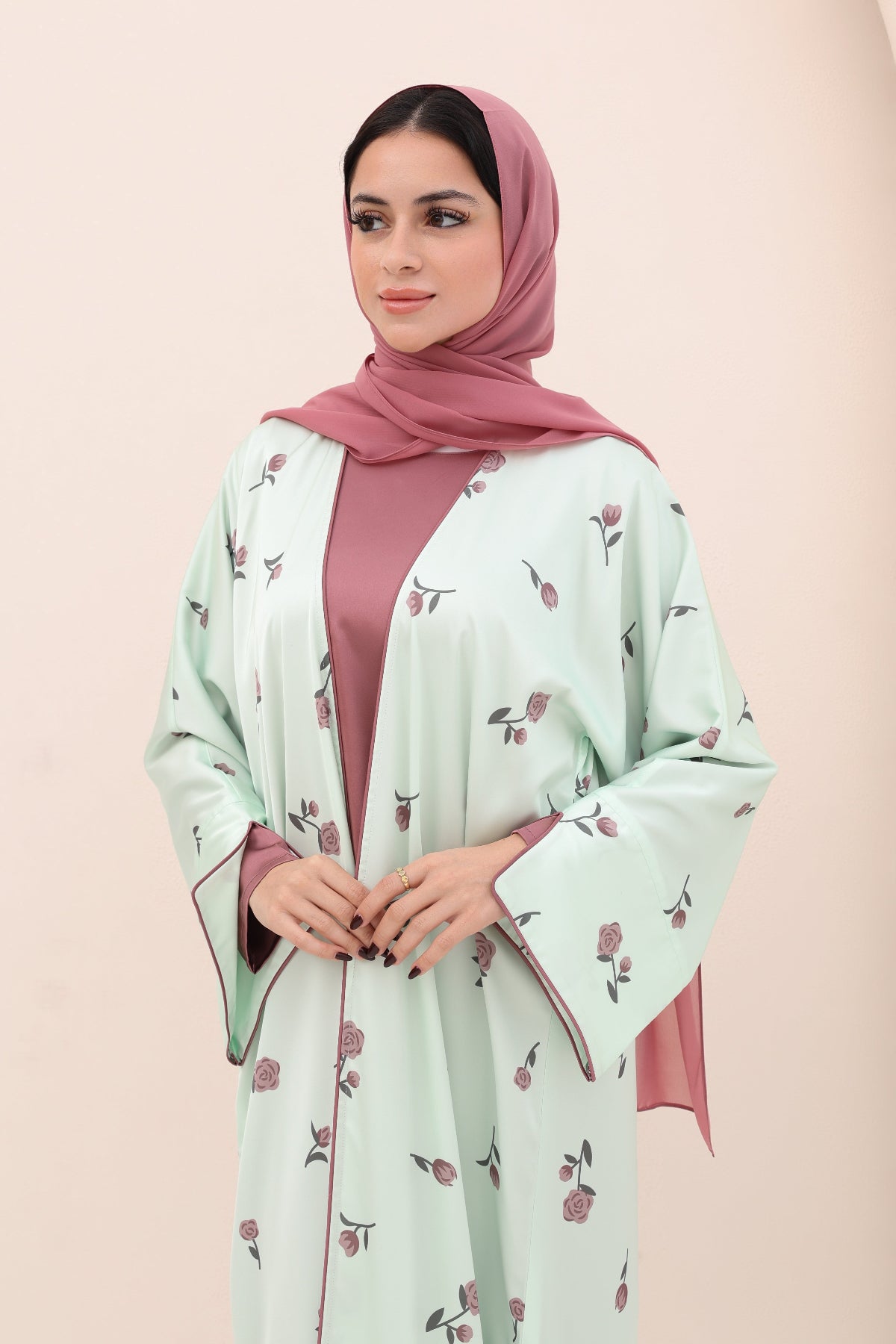 Woman wearing a light green floral dress with a pink hijab on a beige background