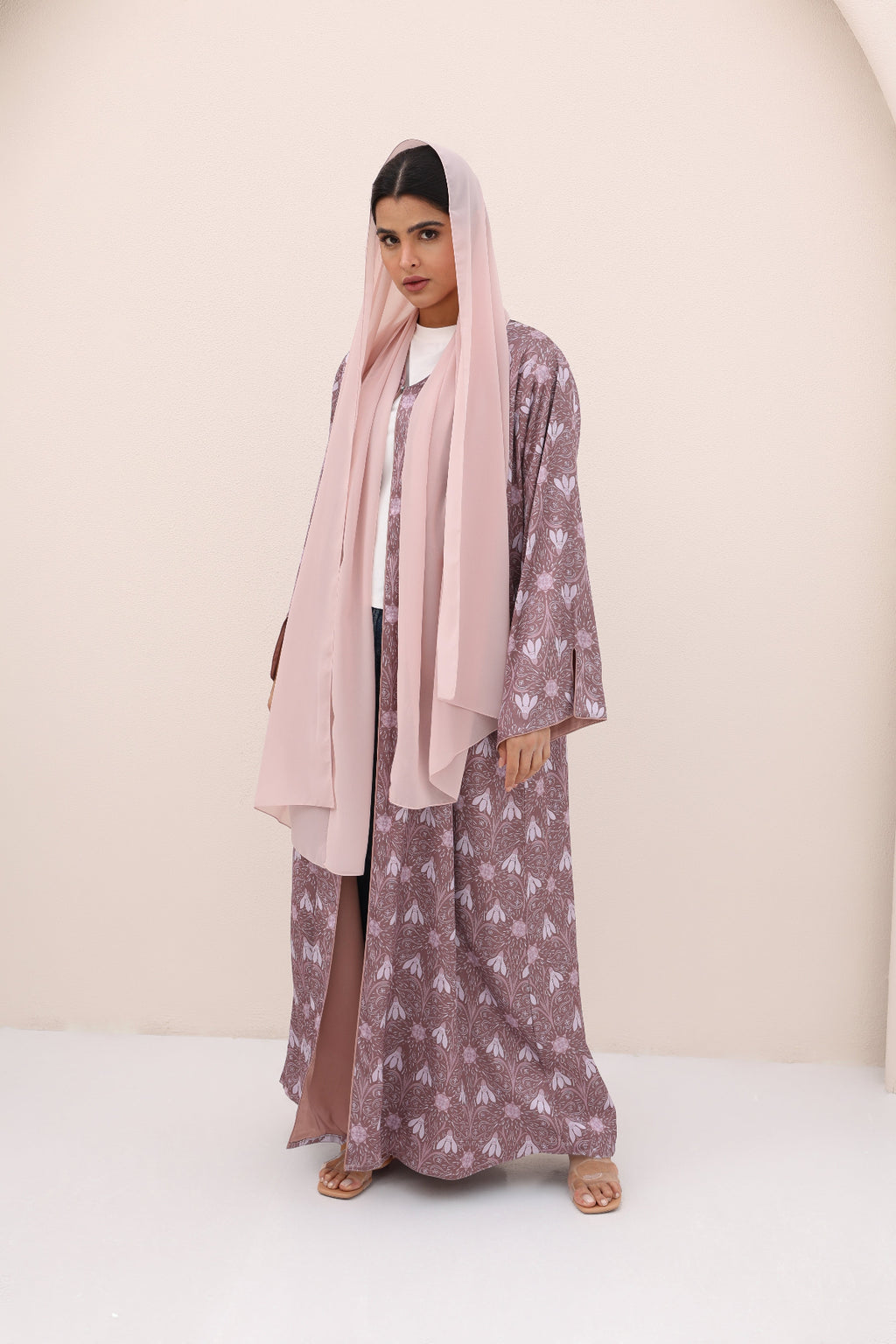 Woman wearing a patterned dress with a pink hijab against a plain background