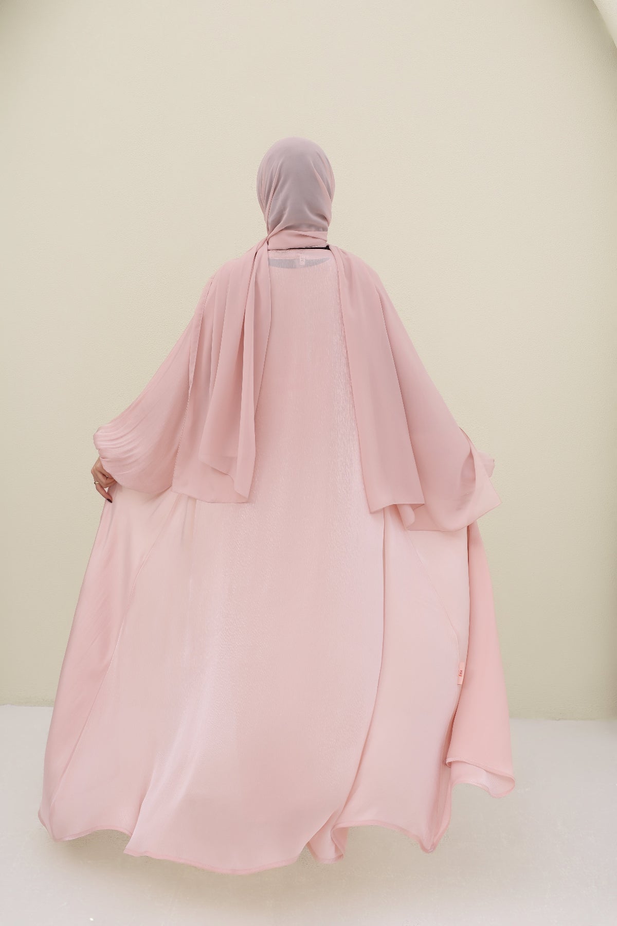 Person wearing a pink abaya and hijab against a plain background