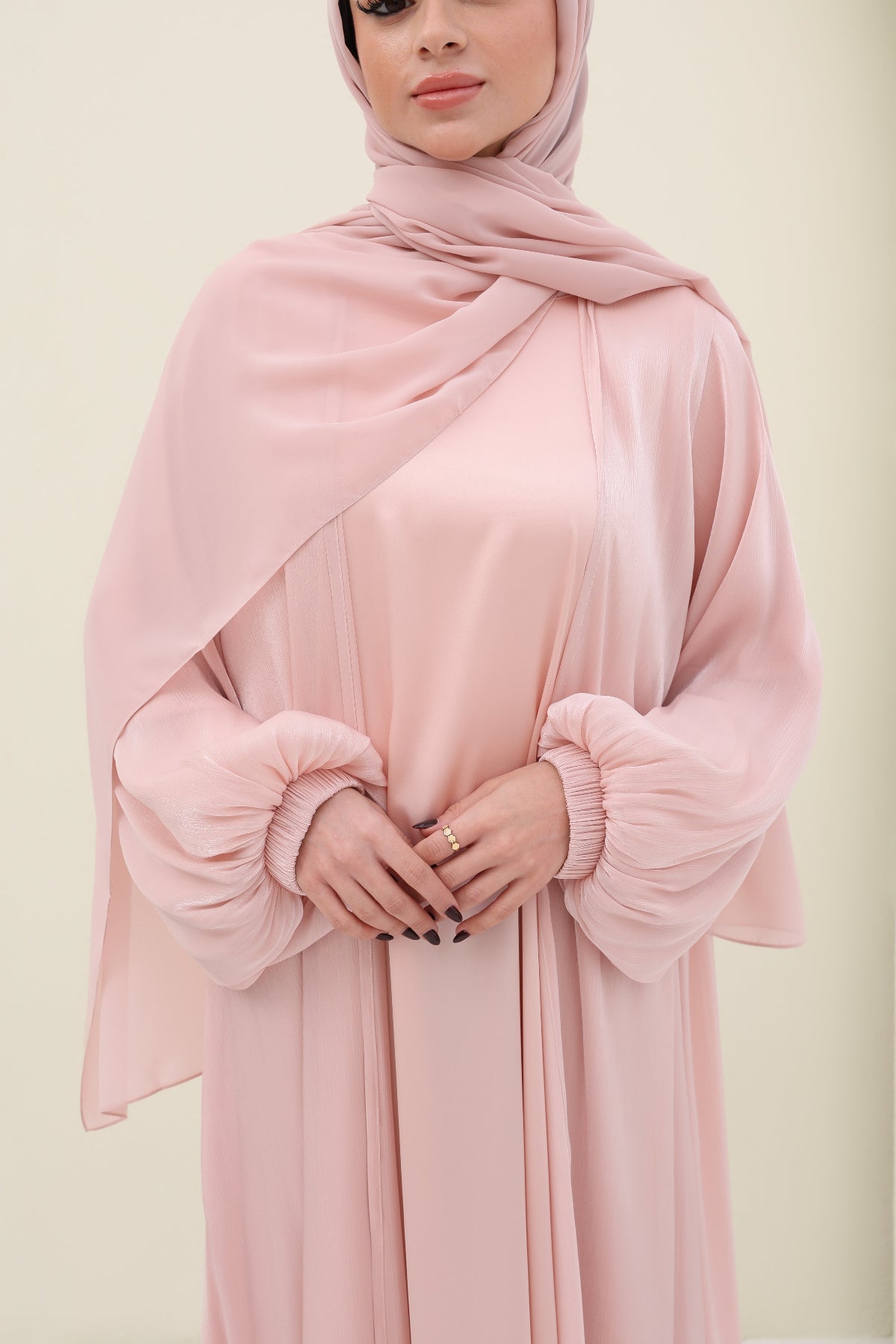 Woman wearing a pink abaya with a matching hijab on a light beige background