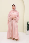Woman wearing a pink abaya with a matching hijab against a plain background