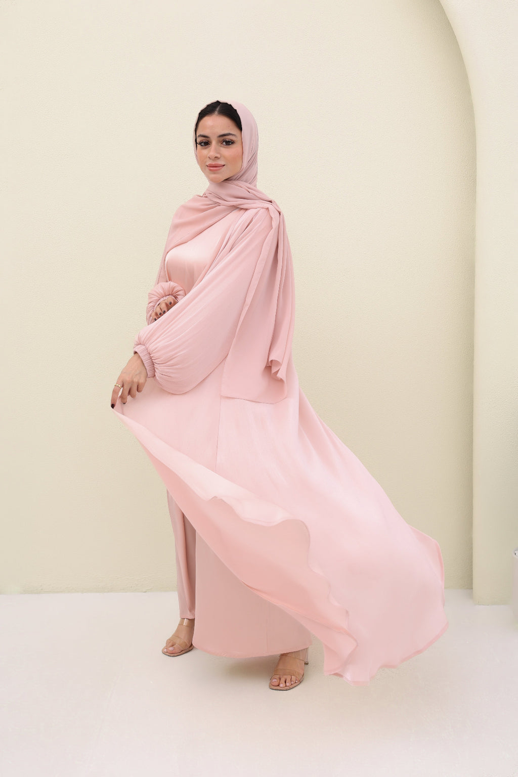 Woman wearing a pink abaya against a plain background