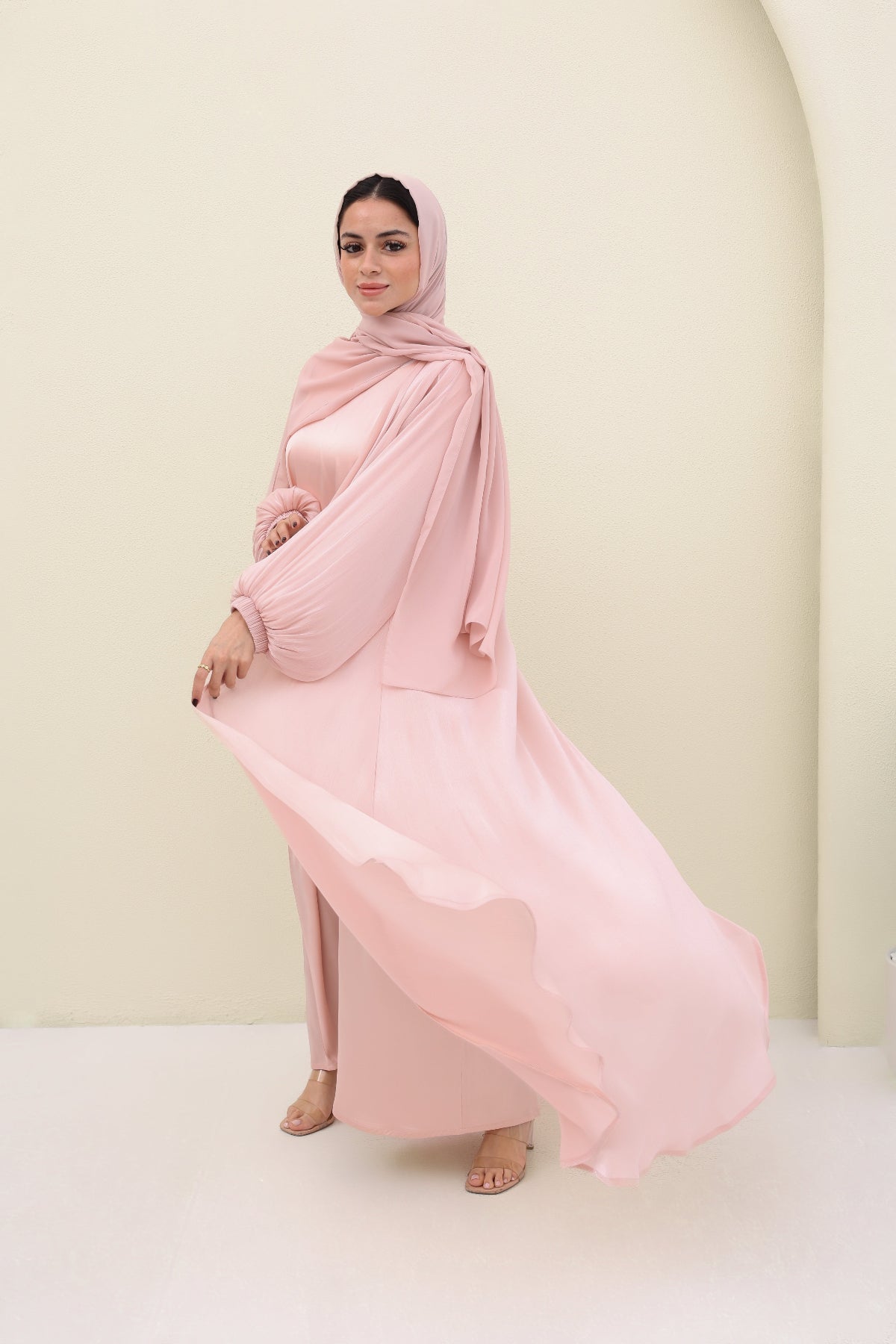 Woman wearing a pink abaya against a plain background