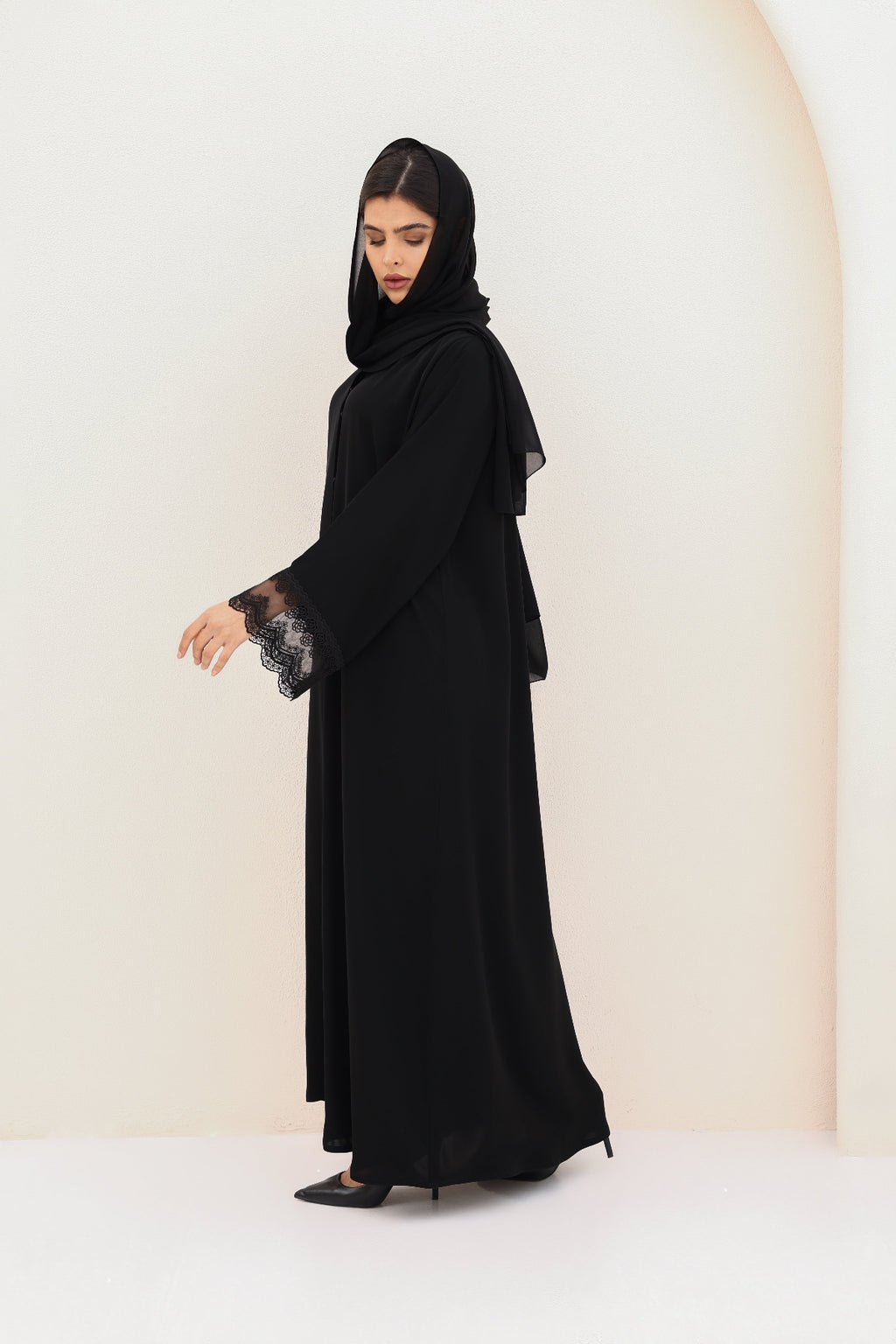 Woman wearing a black abaya with lace sleeves on a white background