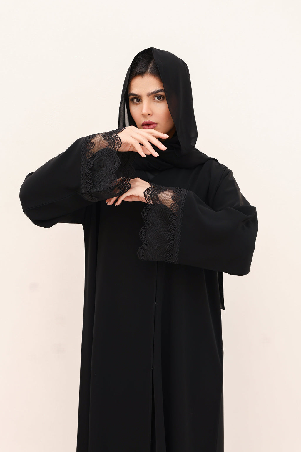 Woman wearing a black abaya with lace details on a white background