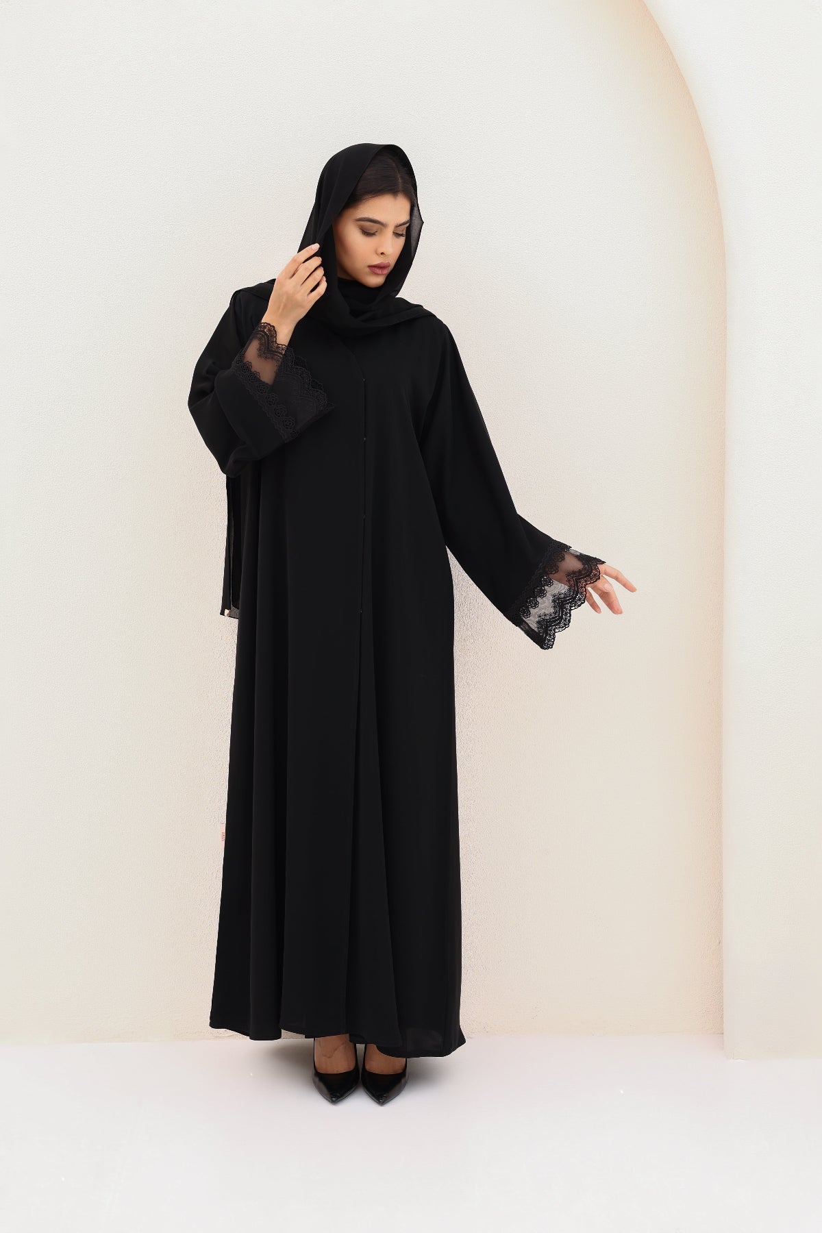 Woman wearing a black abaya with lace sleeves against a white background