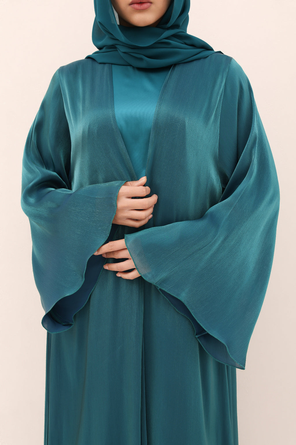 Teal abaya worn by a person on a beige background