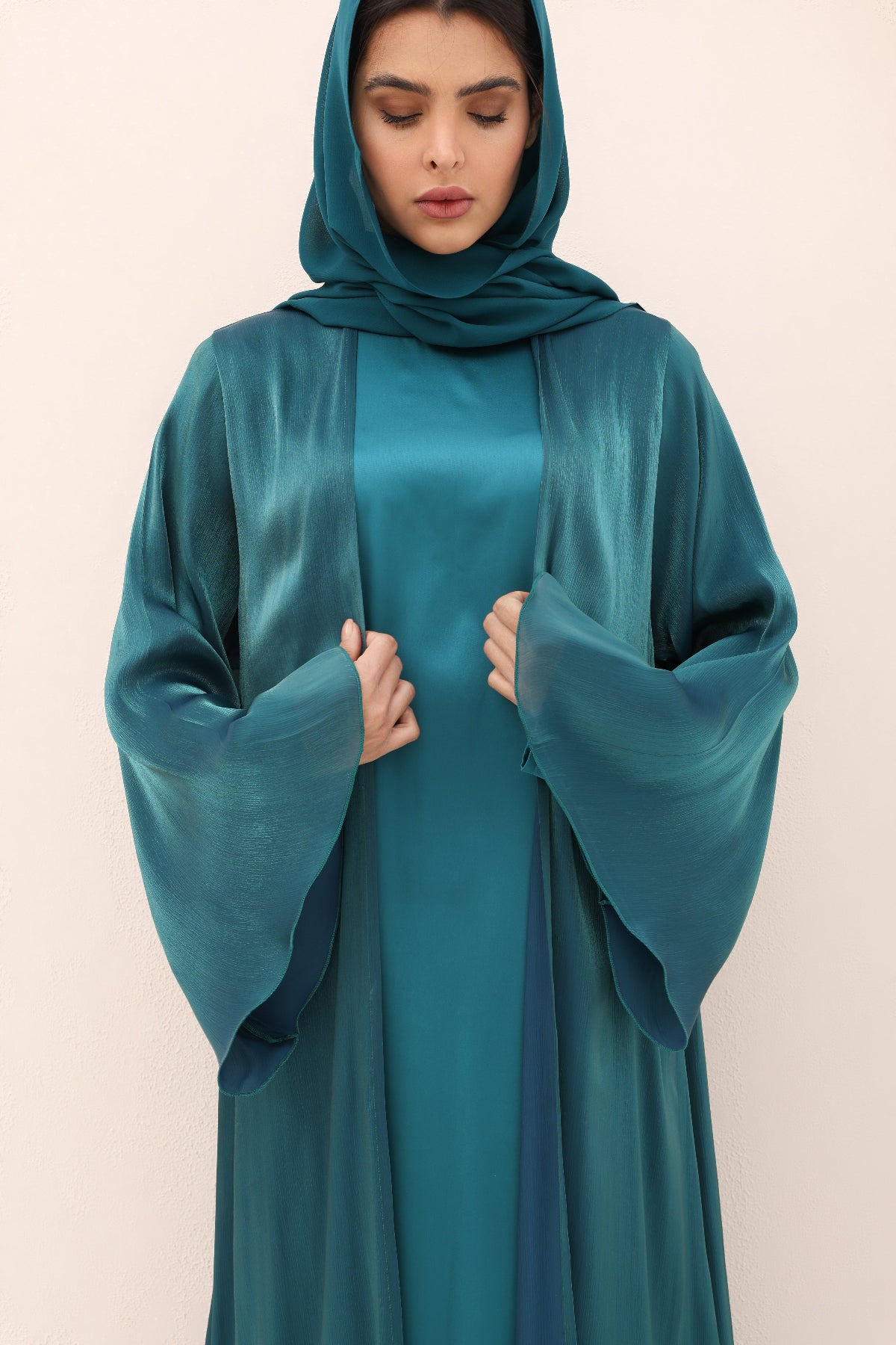 Woman wearing a teal abaya against a beige background