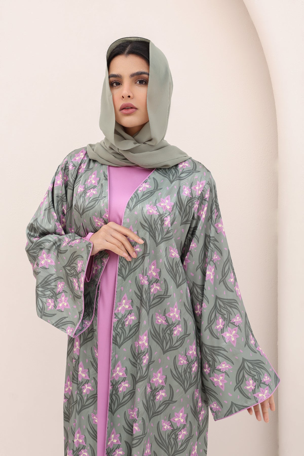 Woman wearing a gray floral-patterned abaya over a pink dress against a beige background