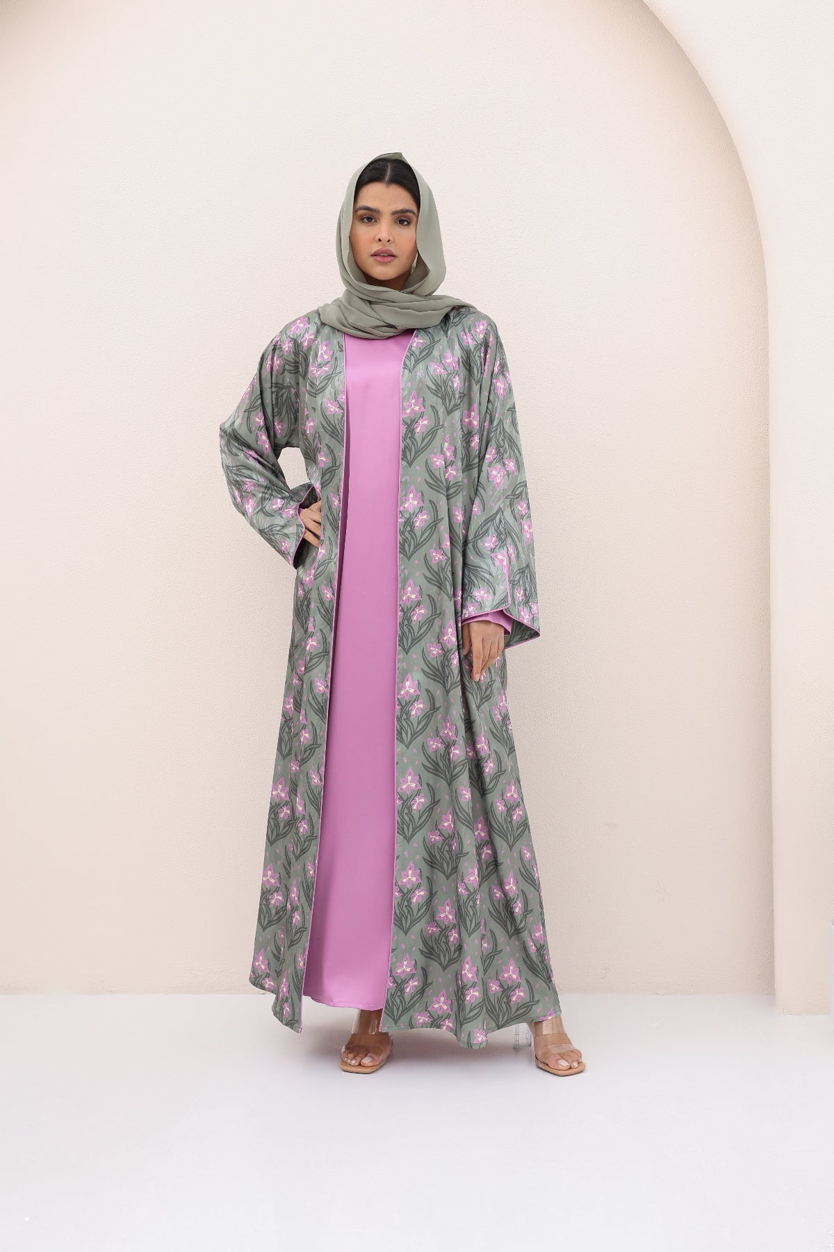 Woman wearing a floral abaya over a pink dress against a beige background