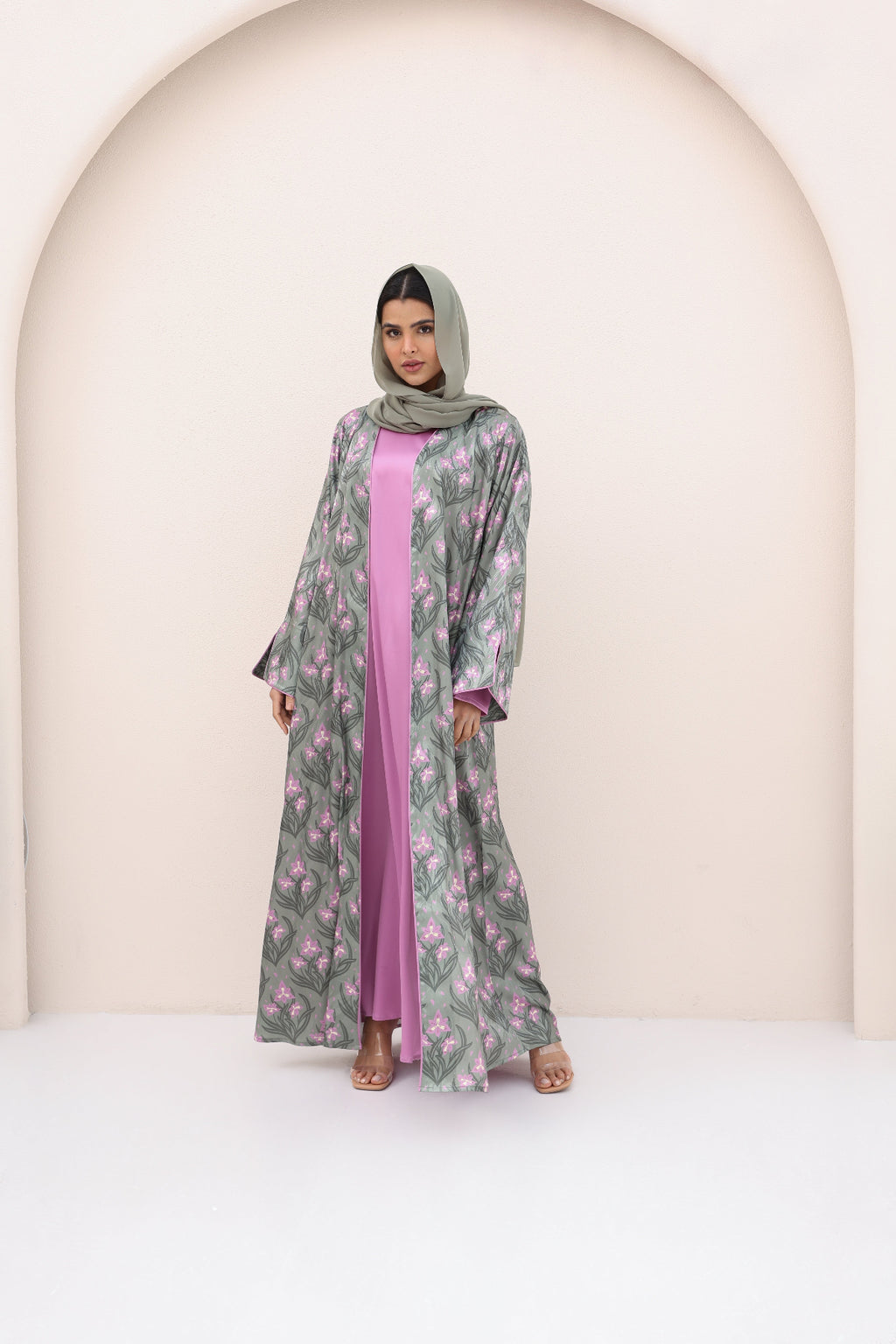 Woman wearing a floral abaya with a pink inner garment against a neutral background
