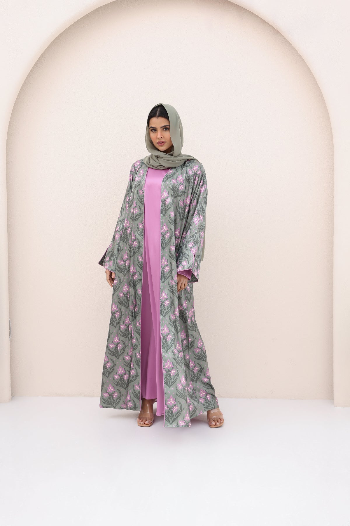 Woman wearing a floral abaya with a pink inner garment against a neutral background